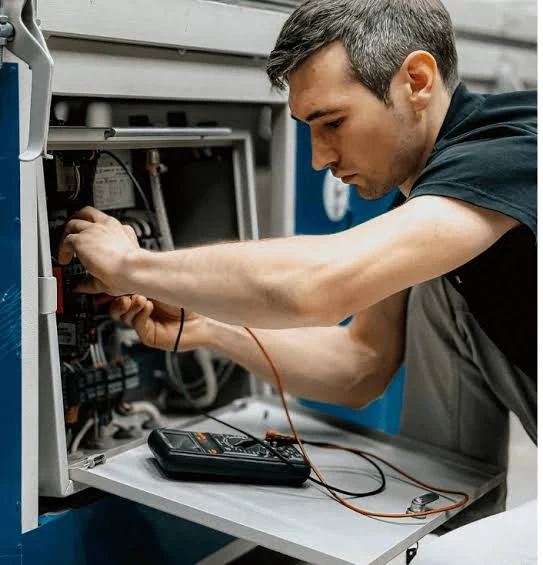 Technician inspecting electrical components inside an HVAC system with a digital multimeter