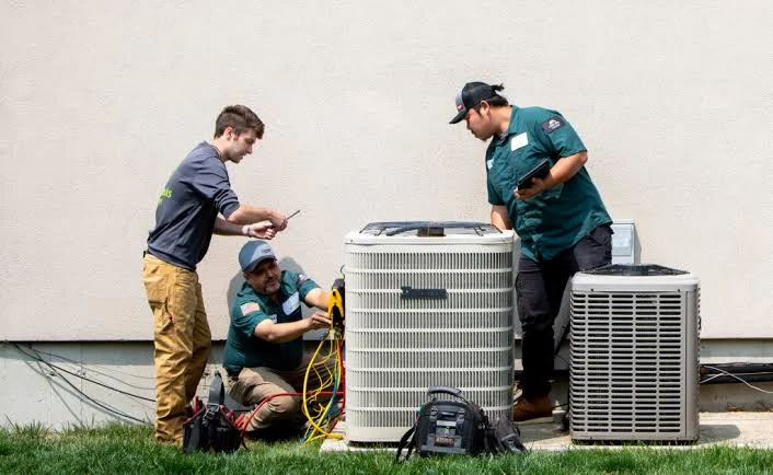 Three technicians inspecting residential outdoor air conditioning equipment